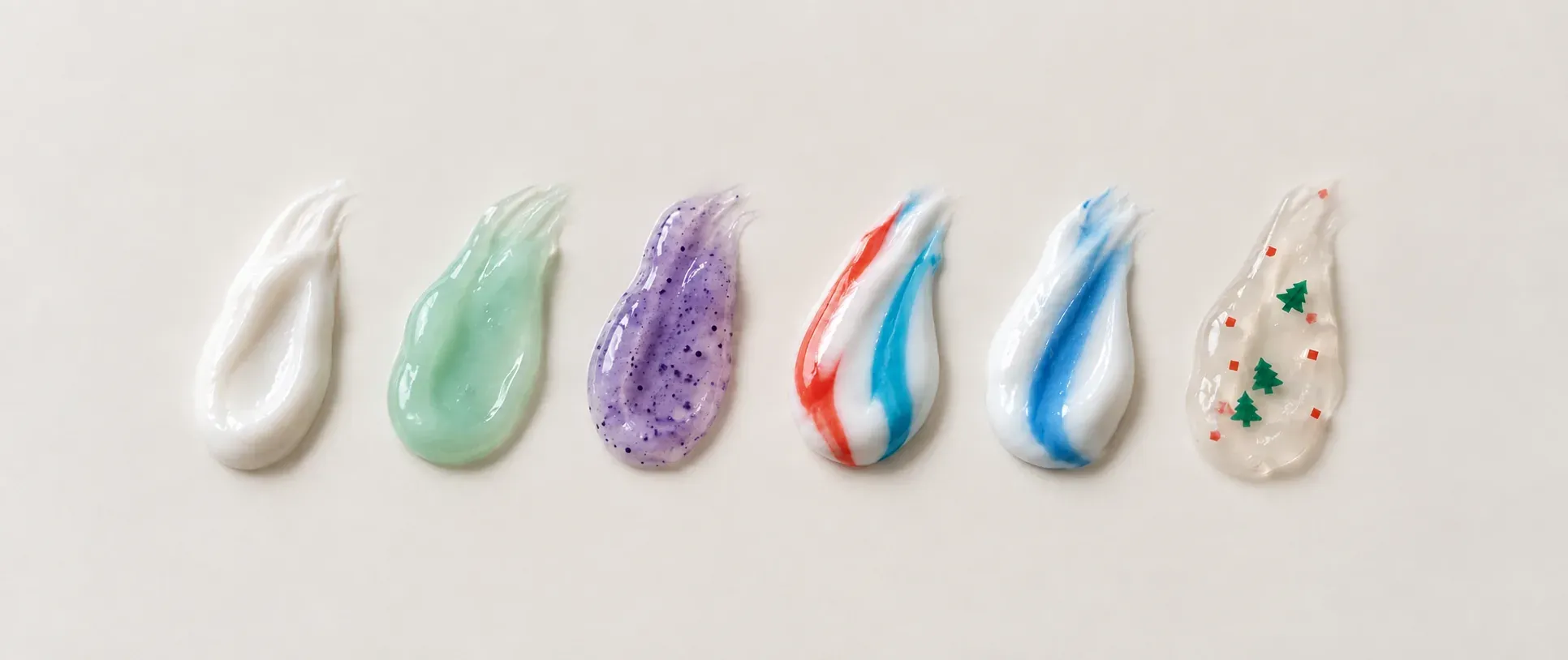 Six toothpaste swatches showing white paste, green and purple gels, colored stripes and a clear gel with flakes.