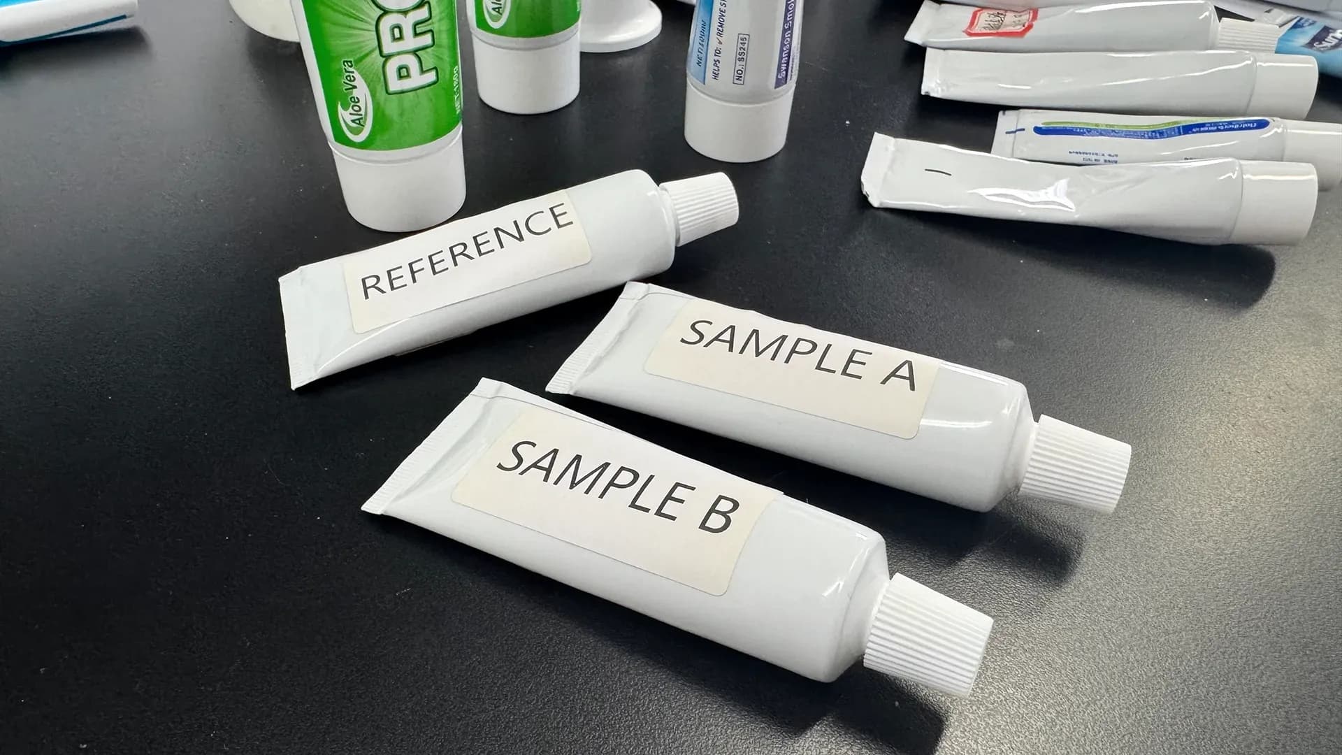 Tubos reales de pasta dental con las etiquetas REFERENCE, SAMPLE A y SAMPLE B sobre una mesa de trabajo.