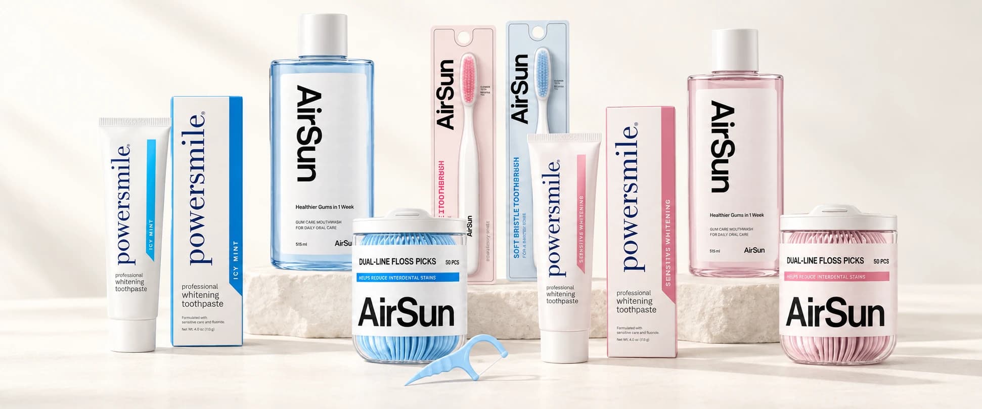 Pasta dental, enjuague bucal, cepillos y palillos con hilo dental en azul y rosa pálido, dispuestos sobre una base color marfil.