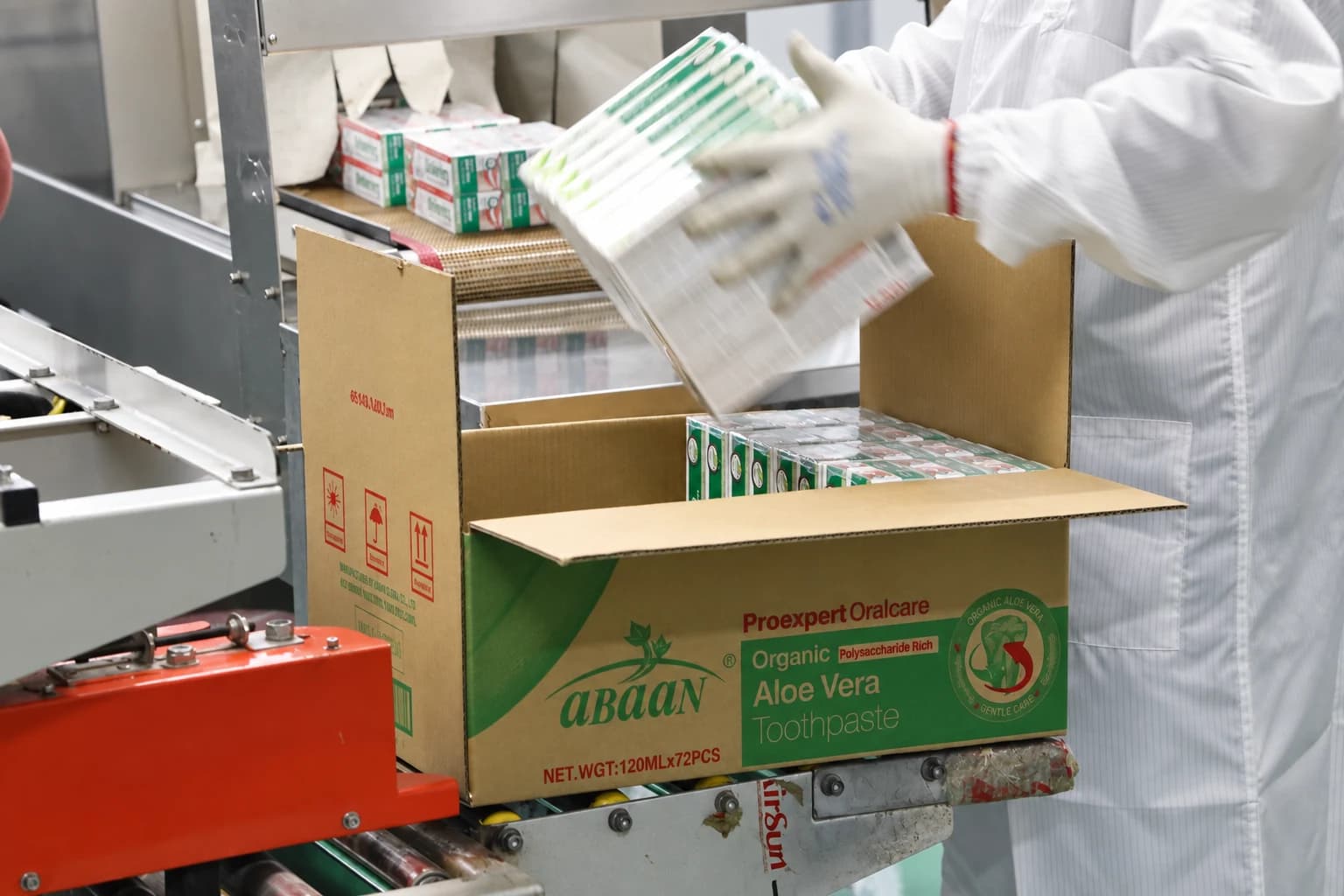 Un operario coloca cajas de pasta dental en una caja de transporte en la línea de producción.